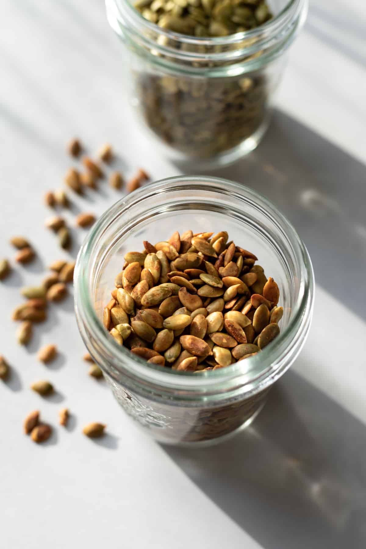 glass jar of toasted pumpkin seeds with raw seeds in background