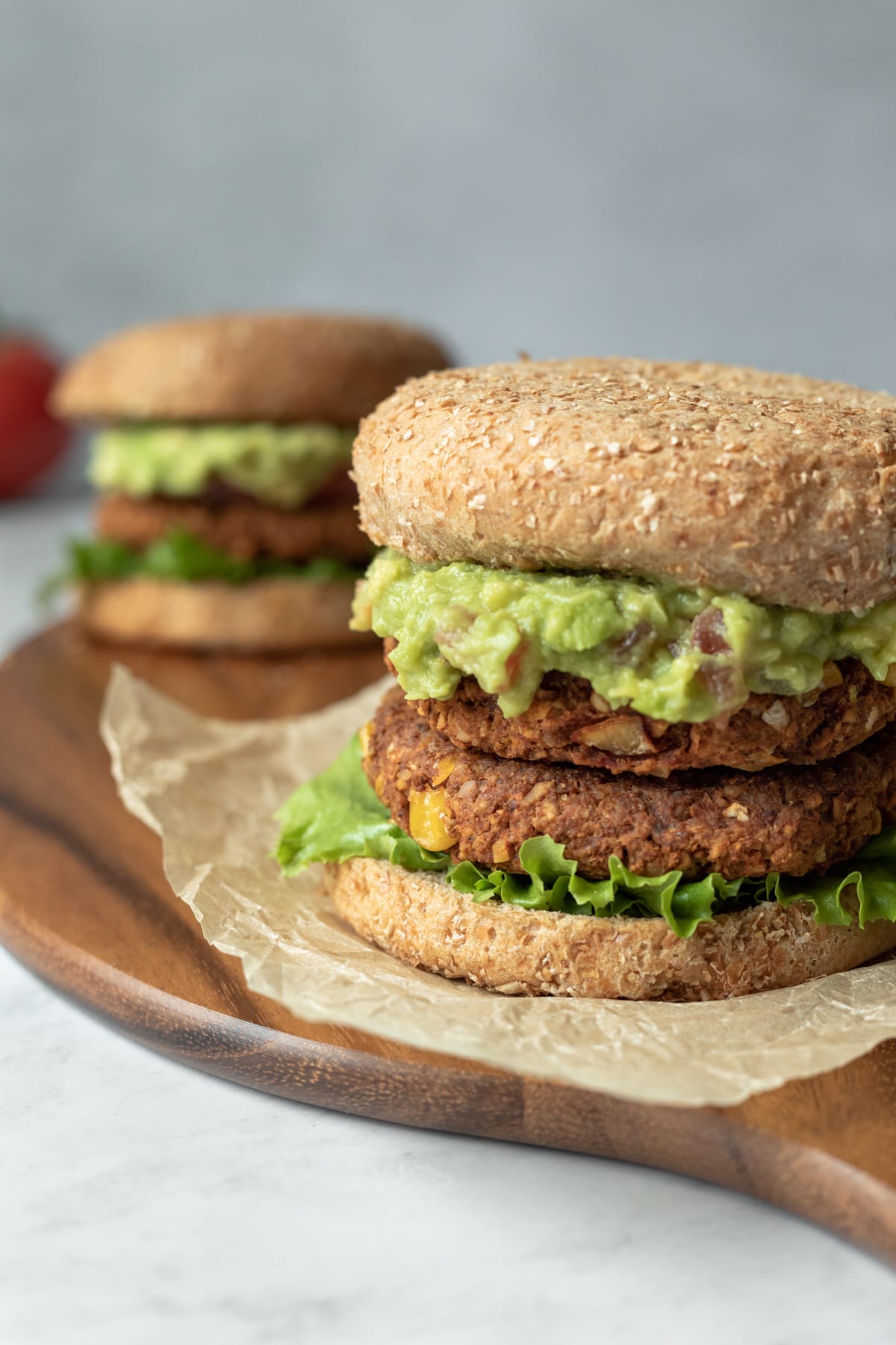 two vegan burgers loaded with fixings sitting on a wood serving board.