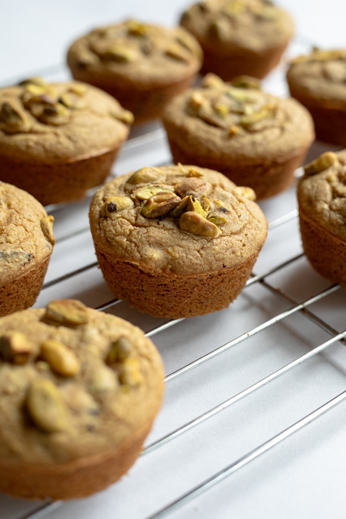 muffins with pistachios on top on a cooling rack.