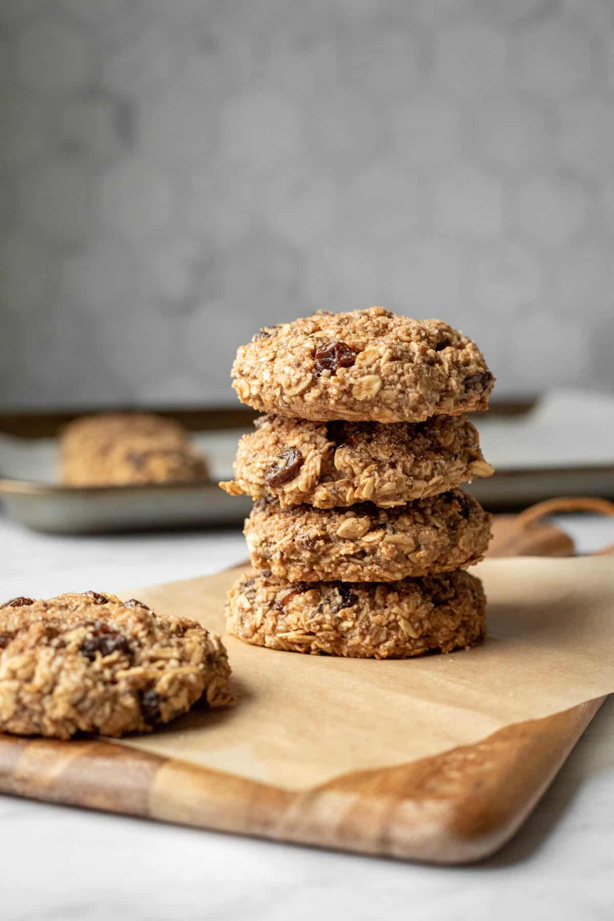 Thick vegan breakfast cookies stacked on a wood board against a gray tile background.