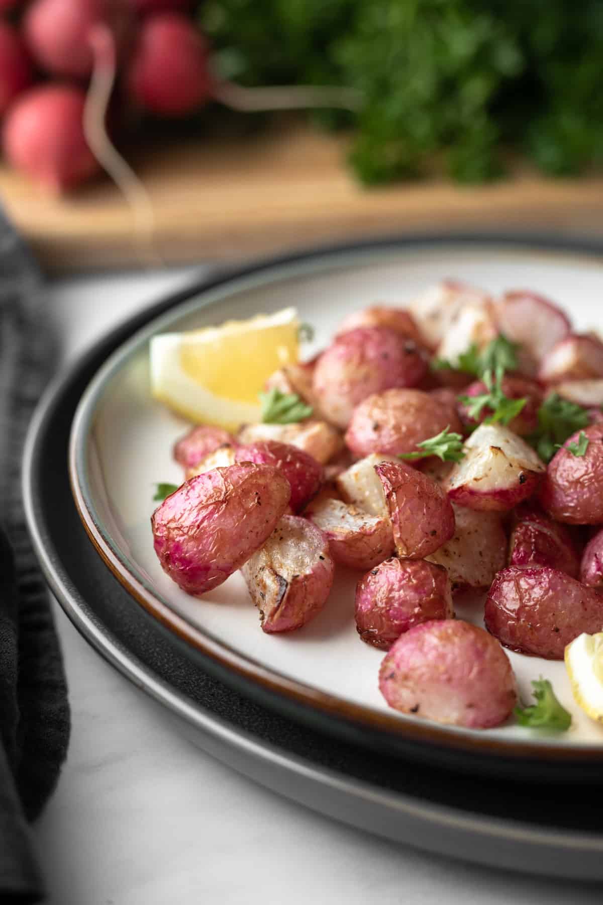 air fried radishes on a white plate with bunch of parsley in background.