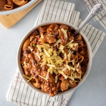 thick chili mac in a white bowl topped with shredded vegan cheese