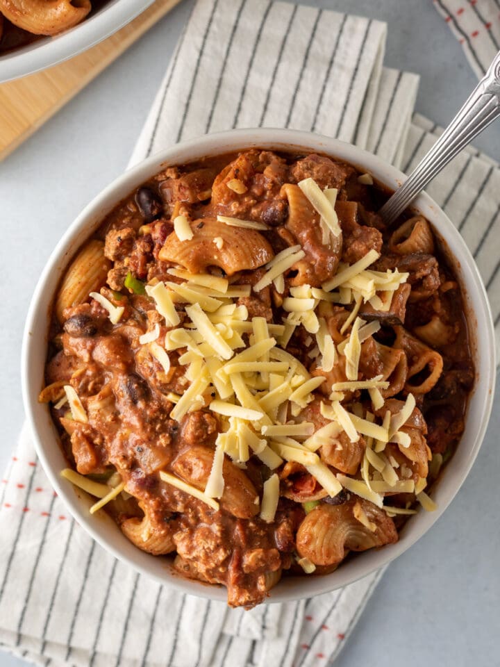 thick chili mac in a white bowl topped with shredded vegan cheese