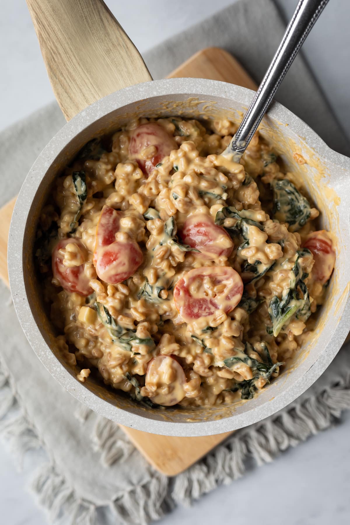 creamy farro dish in pot with colorful tomatoes and kale