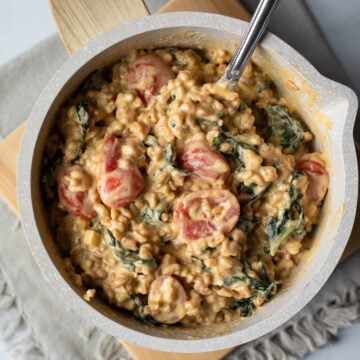 close up of creamy and cheesy farro mixed with kale and tomatoes in a small pot