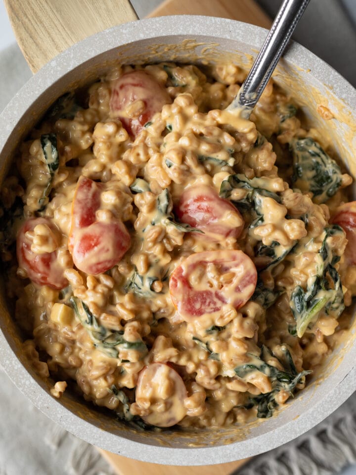 close up of creamy and cheesy farro mixed with kale and tomatoes in a small pot