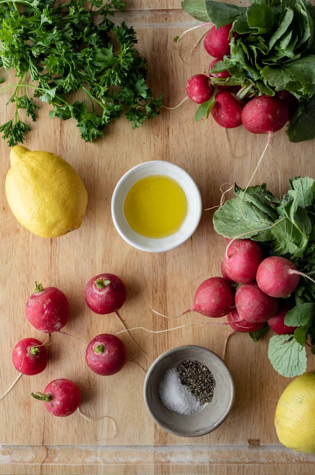 ingredients laid out on a wood cutting board - radishes, lemon, oil, parsley, salt, pepper.