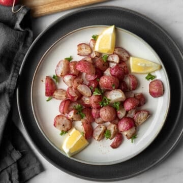 cooked radishes on a white plate garnished with lemon and parsley