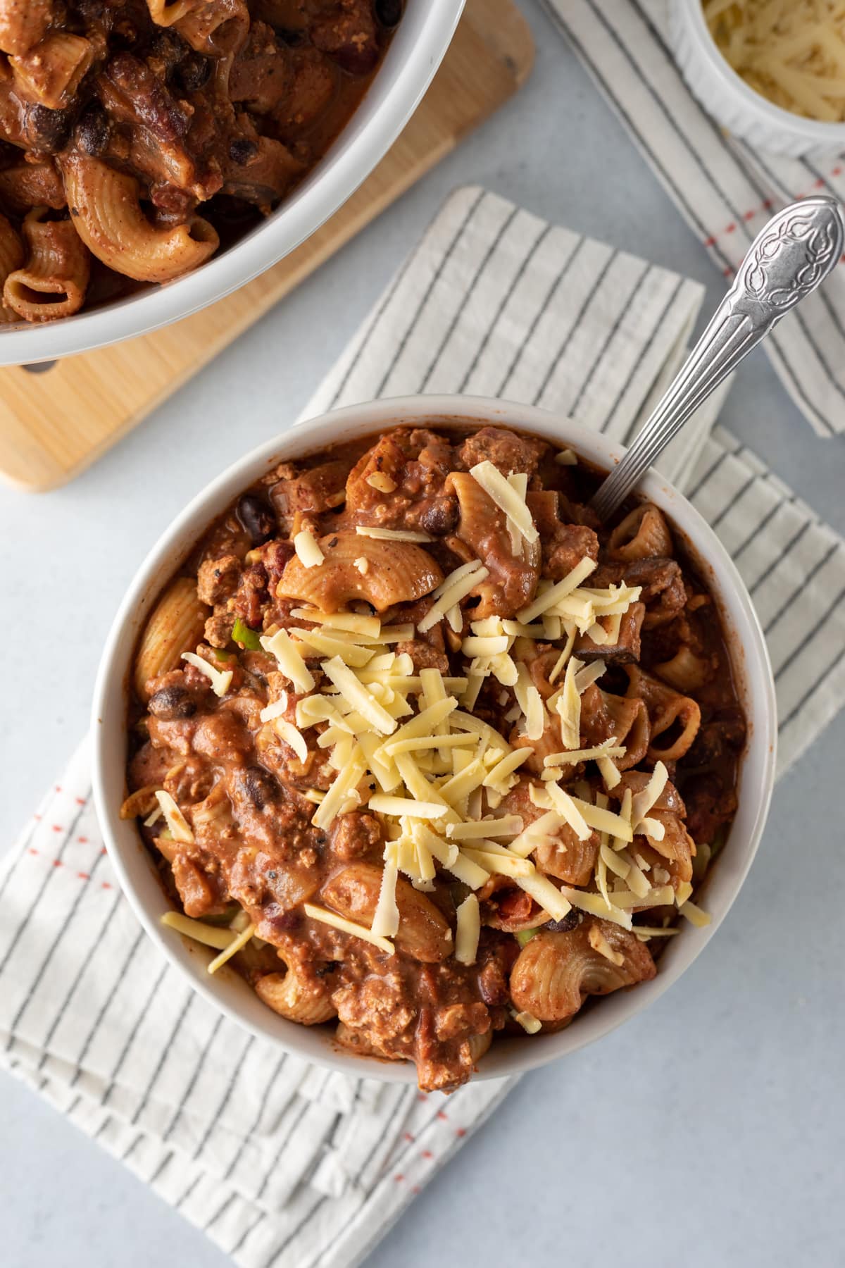 A serving of chunky vegan chili mac topped with shredded cheese.