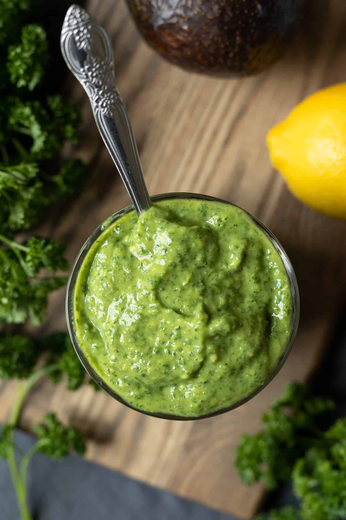 close up of creamy goddess dressing in a glass with a spoon stuck into the center.