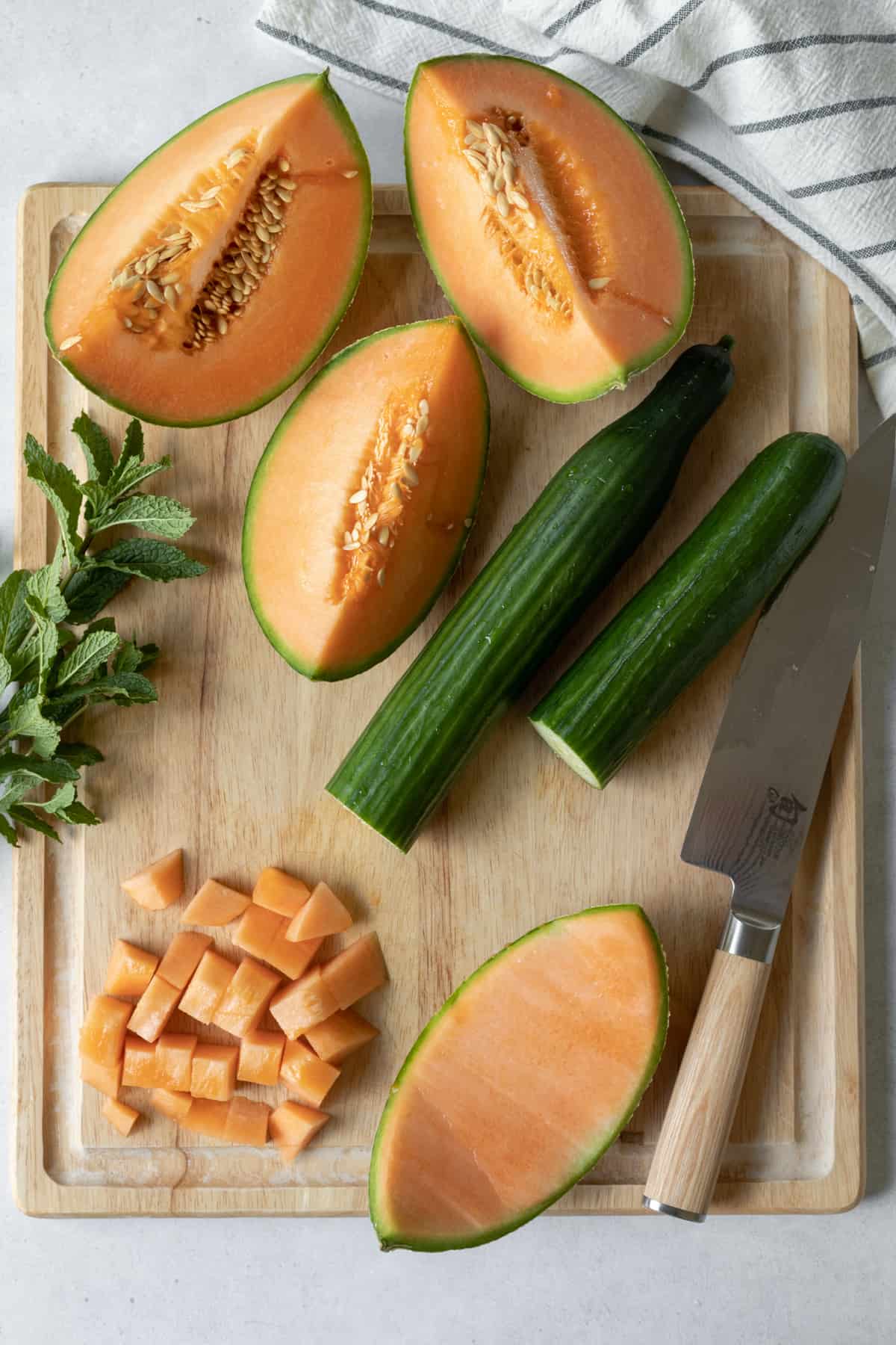 cantaloupe and cucumber on cutting board with a knife, demonstrating size of cubed melon.