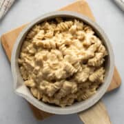 creamy macaroni and cheese in a small pot sitting on a wood trivet