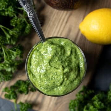 overhead shot of a glass full of creamy goddess dressing with lemon and parsley on the side