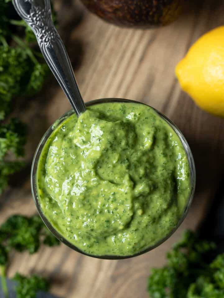 overhead shot of a glass full of creamy goddess dressing with lemon and parsley on the side