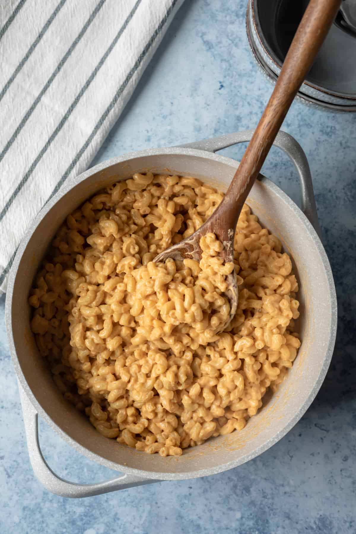 large pot full of mac and cheese and a wooden serving spoon scooping it up.