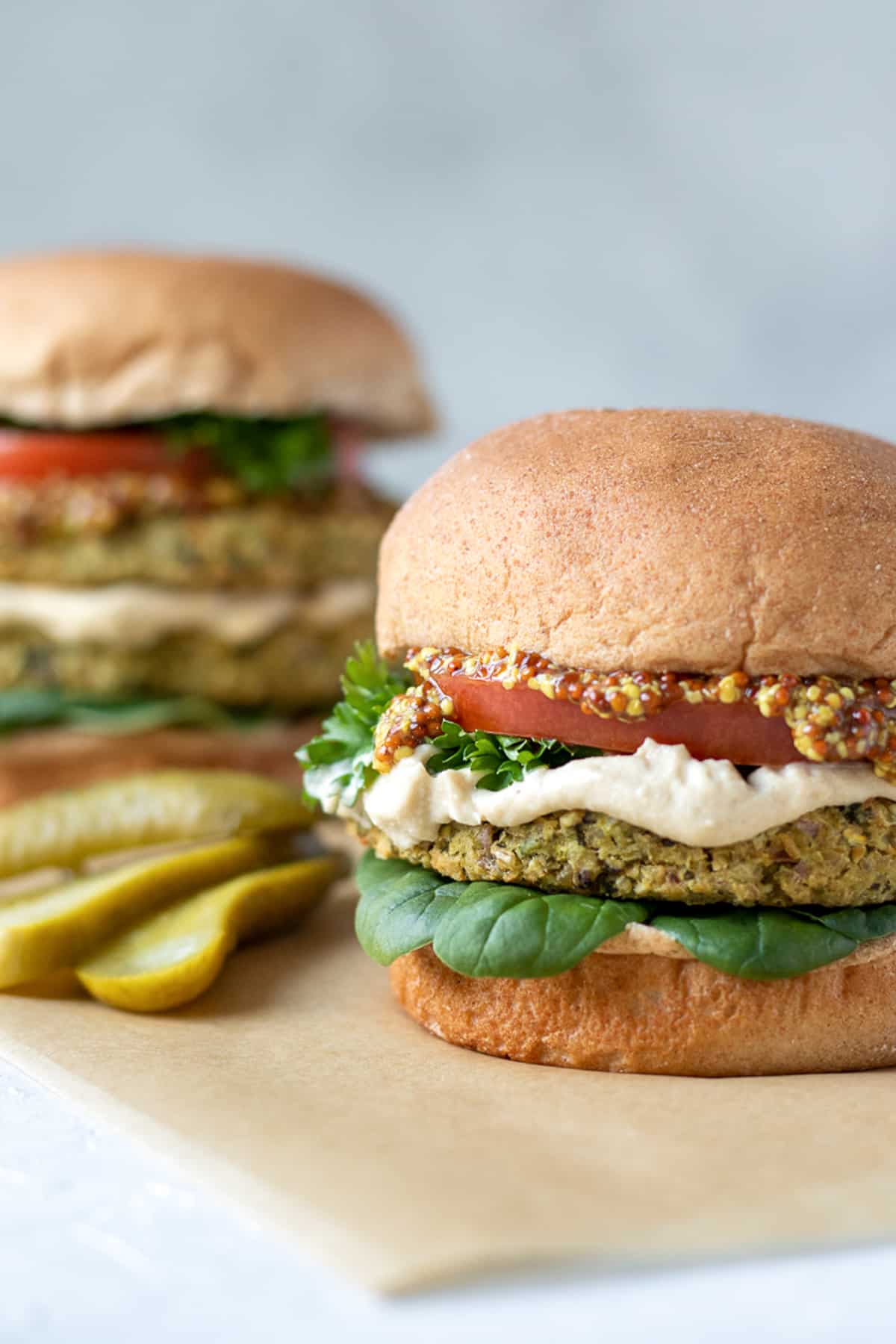 Tabbouleh-Inspired Bean Burgers topped with tomato, parsley, spinach, mustard and hummus.