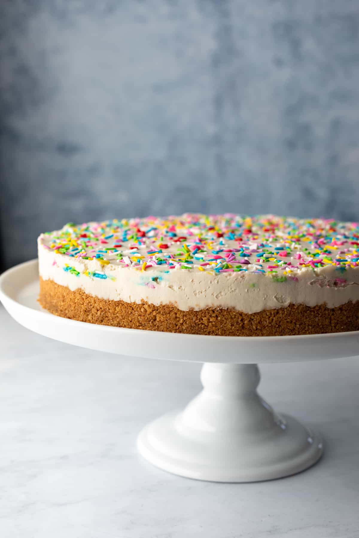 whole cheesecake topped with colorful vegan sprinkles on a white cake stand.