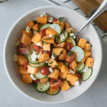 overhead of colorful melon cucumber salad in a large white bowl and garnished with vegan feta