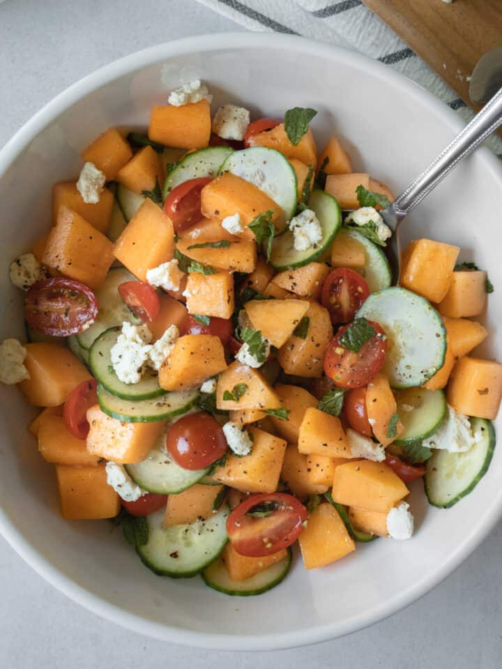 overhead of colorful melon cucumber salad in a large white bowl and garnished with vegan feta