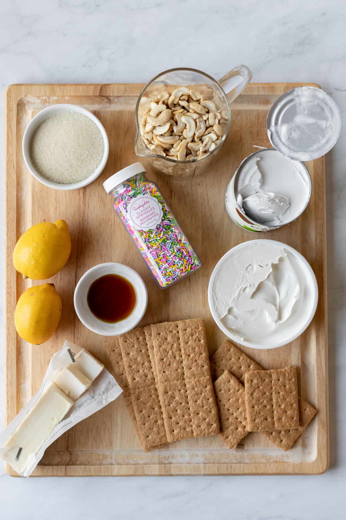 ingredients for vegan cheesecake and graham cracker crust on a wood cutting board.