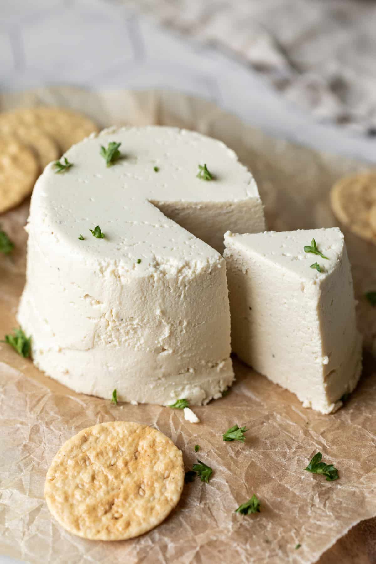 A wheel of tofu-almond feta on parchment paper surrounded by crackers.