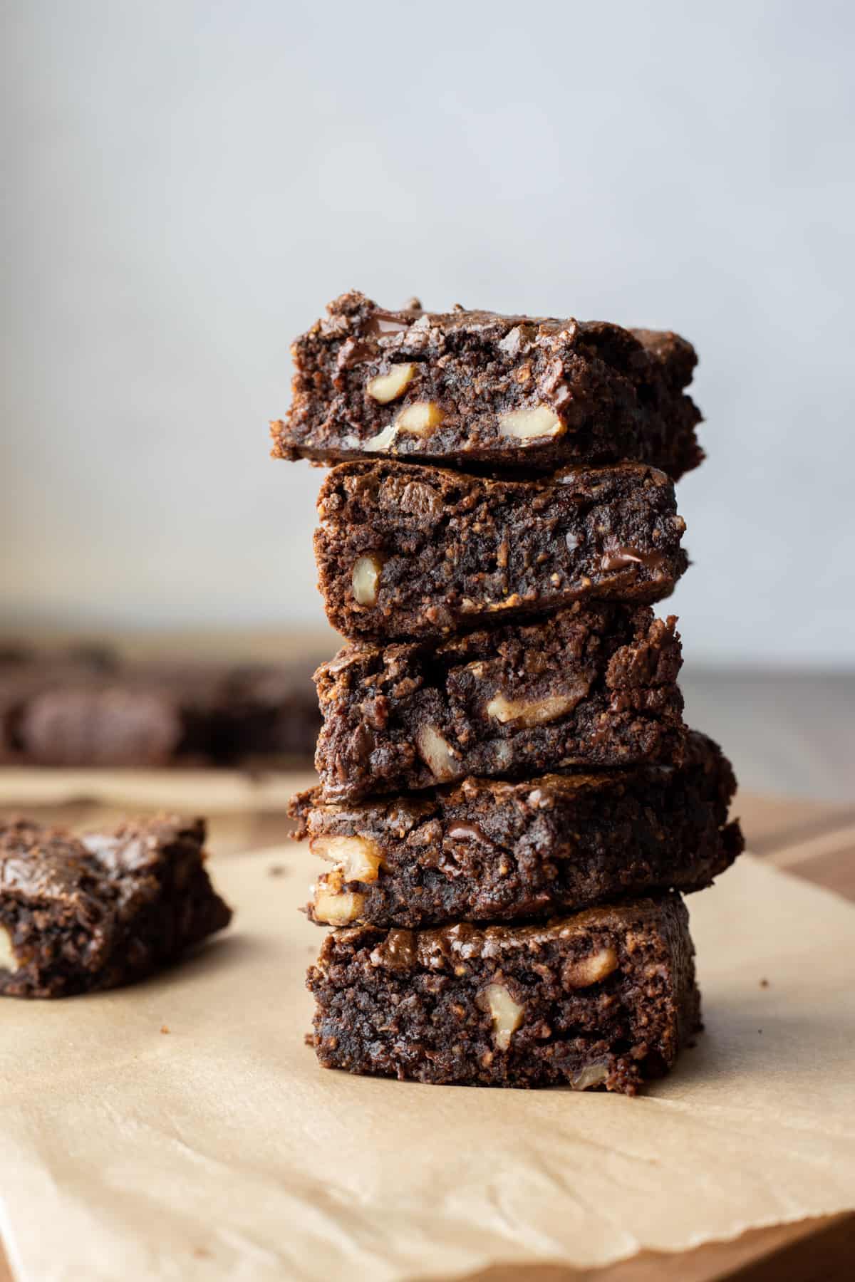 Five dark chocolate brownies with walnuts stacked and resting on a cutting board.
