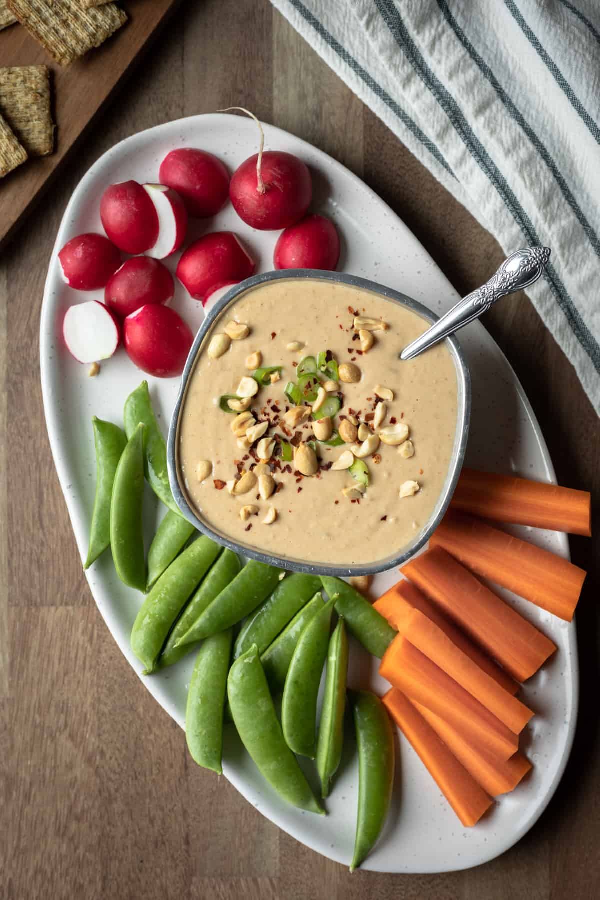 small bowl of vegan peanut dip on a platter surrounded by raw veggies.