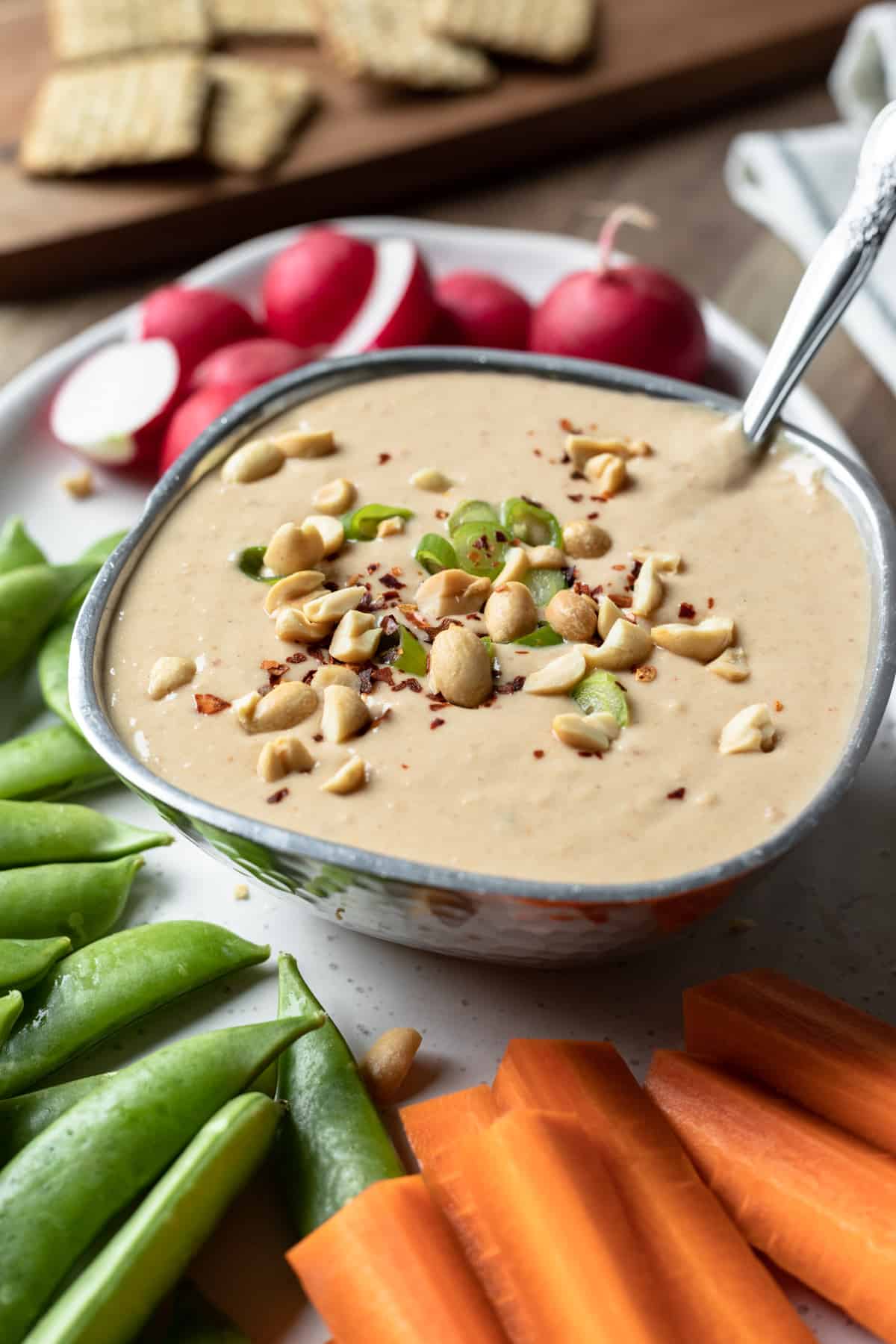 white bean peanut dip in silver bowl surrounded by colorful vegetables.