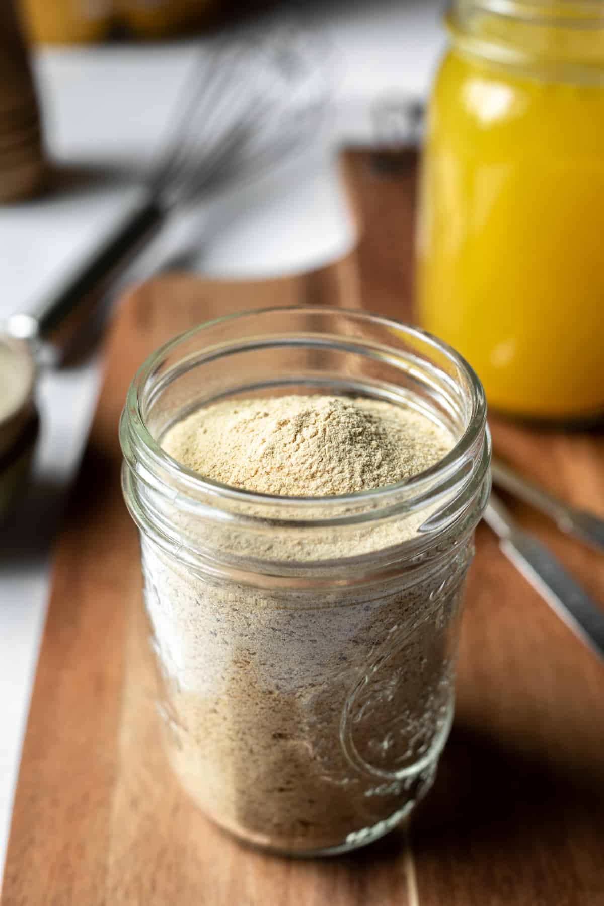 glass jar filled with homemade vegan chicken seasoning with prepared broth in background.