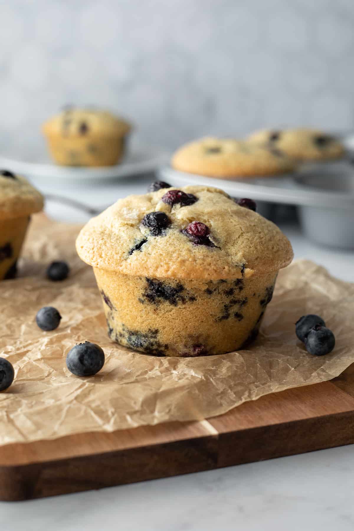 close up of muffin on parchment paper, studded with lots of blueberries.
