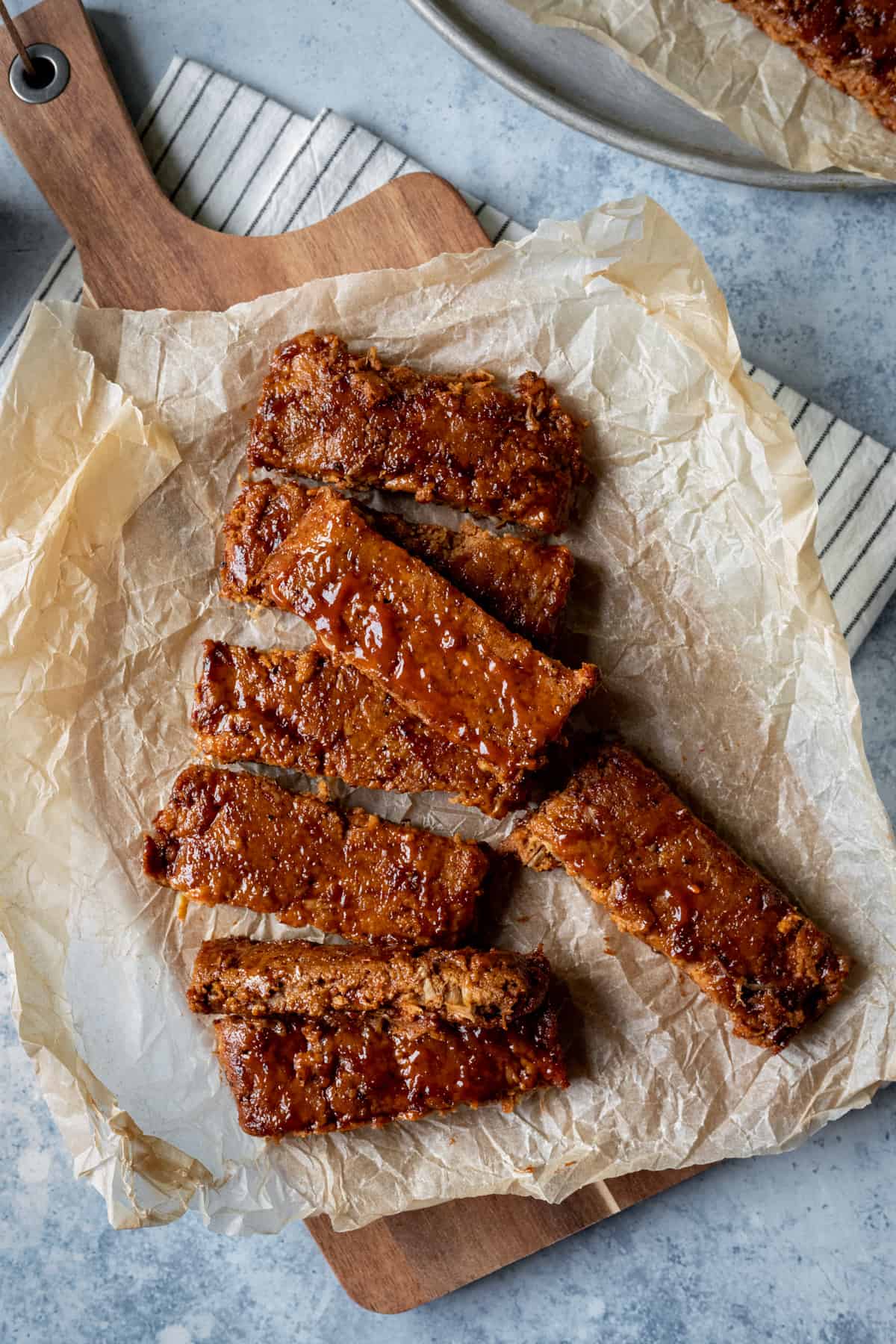 Baked seitan ribs slathered with barbecue sauce on a cutting board.