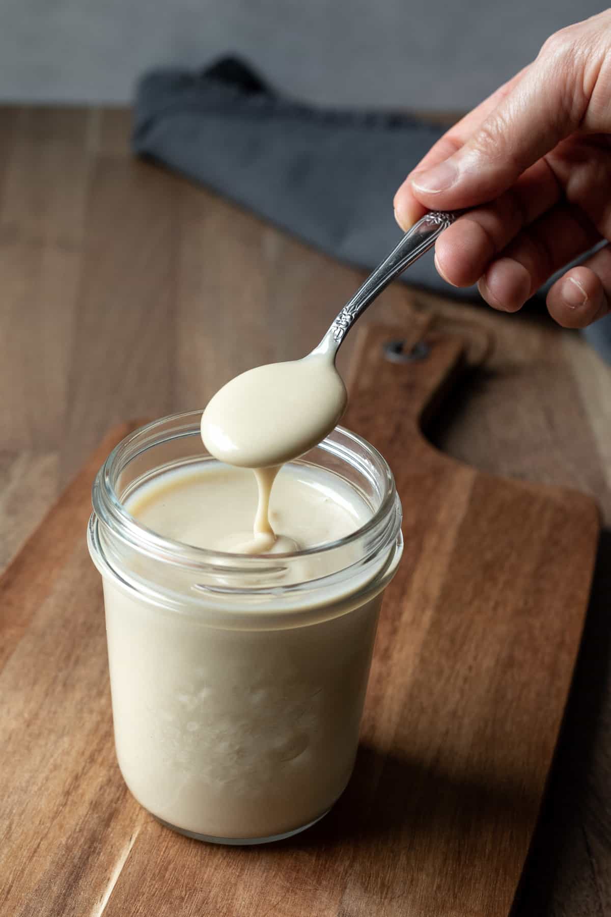 A spoon scooping up thick and creamy dairy-free sweetened condensed milk from a jar.