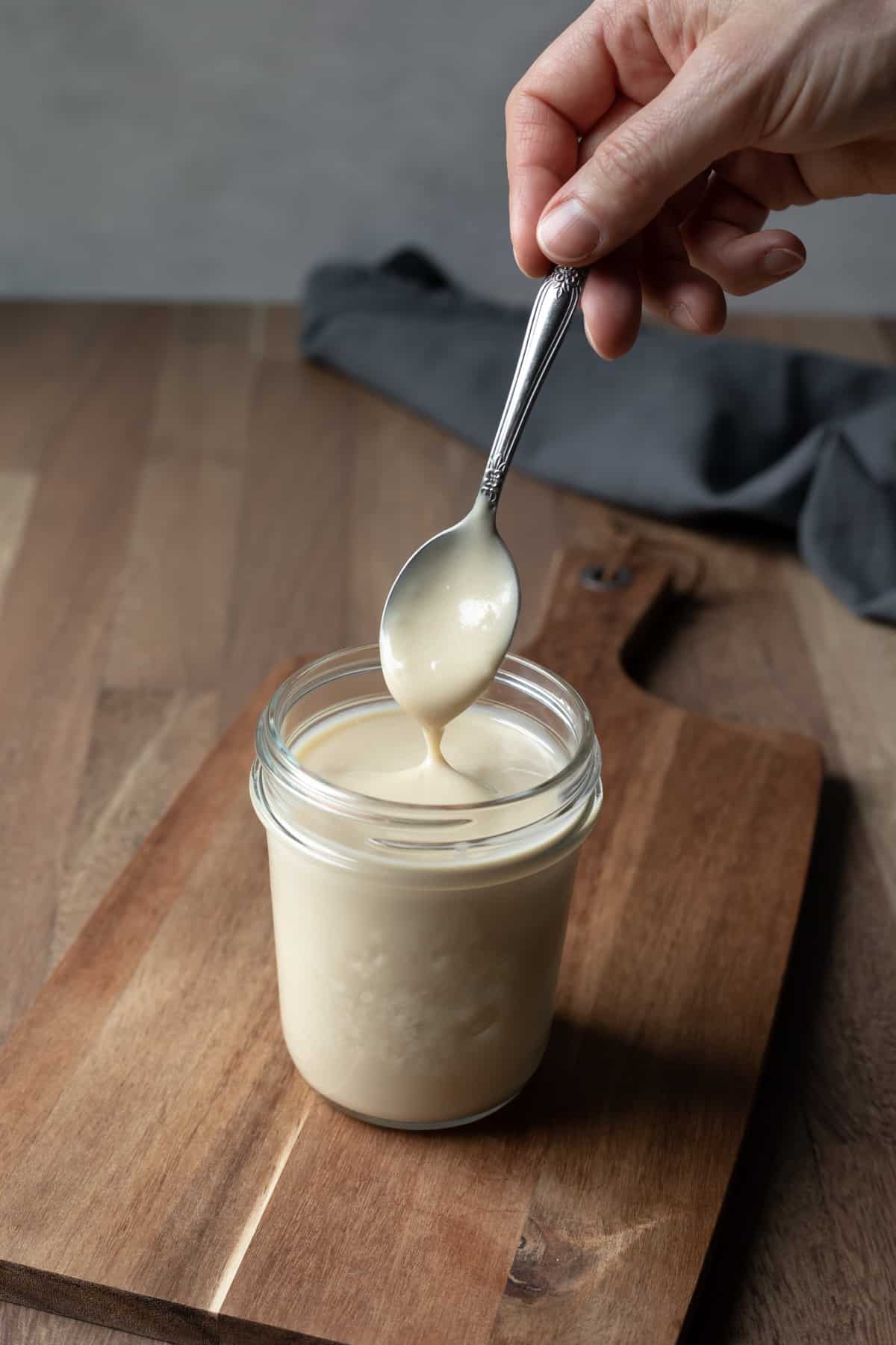 hand lifting a spoon from a glass jar of condensed milk.