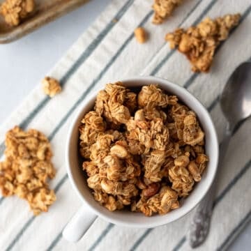 clusters of granola with peanuts in a mug and nearby.