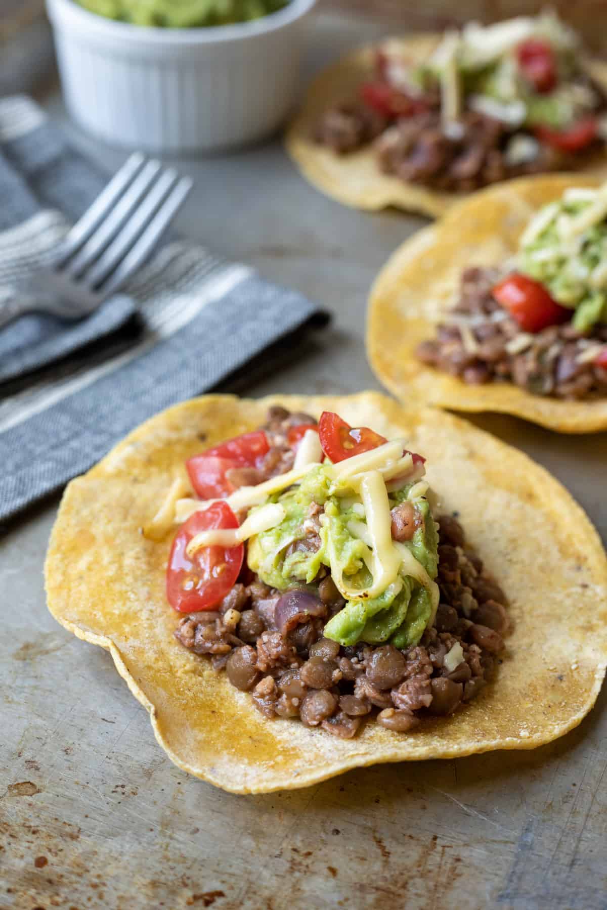 three tacos with lentils, guacamole, cheese, and tomatoes.