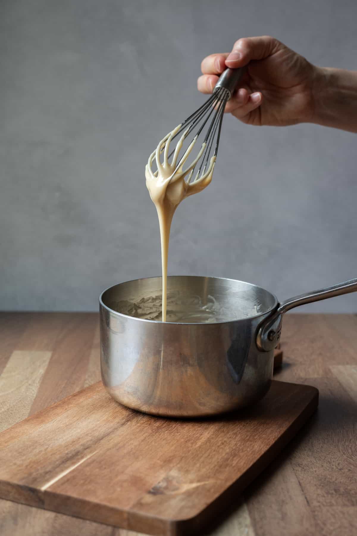 holding a whisk above a pot with thick condensed milk dripping down.