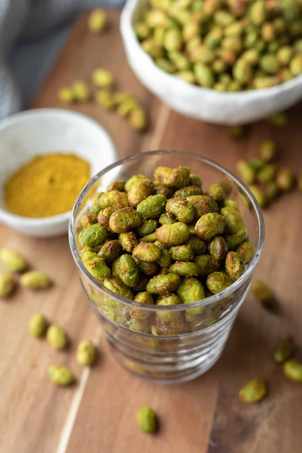 glass full of crunchy air fryer roasted edamame sitting on a wood board.