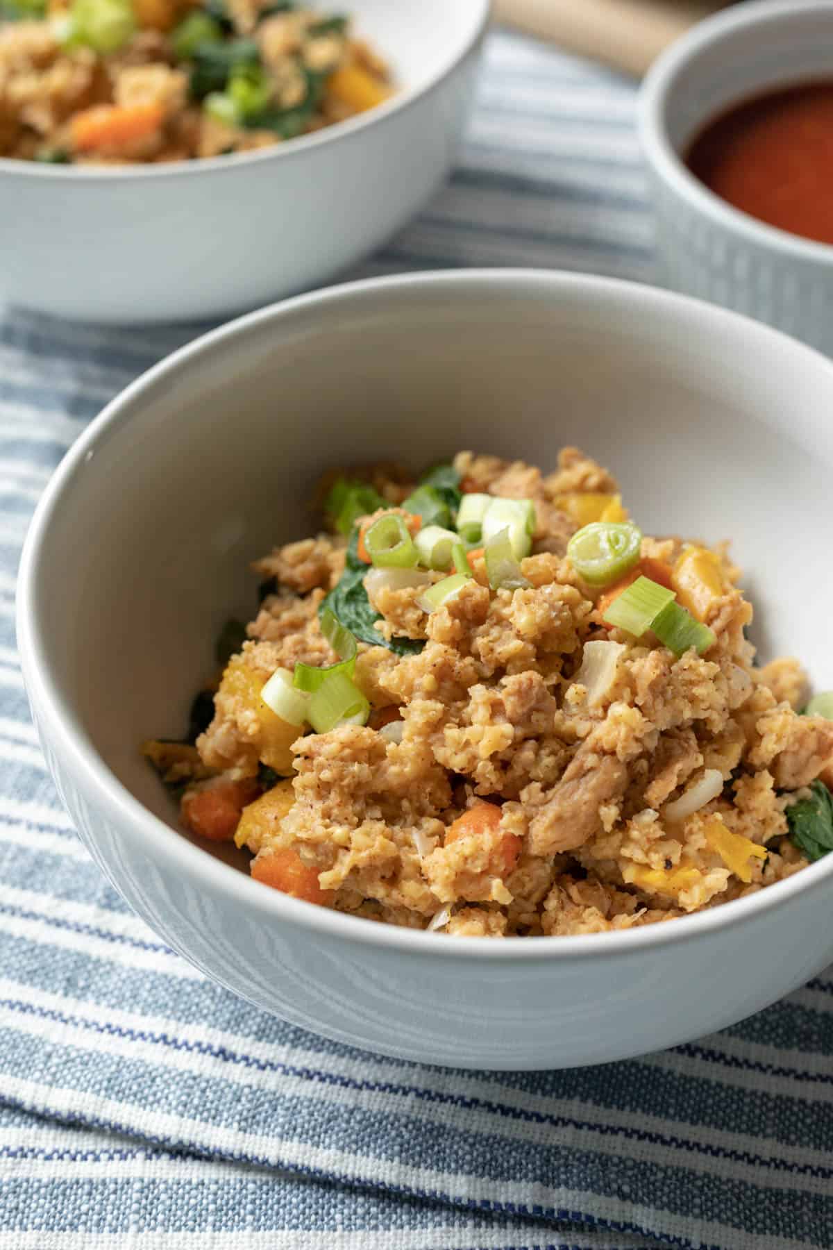 A servine of creamy millet, vegetables, and soy curls in a bowl topped with green onion.