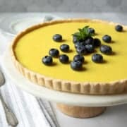 side view of lemon tart on a cake stand against gray tile background.
