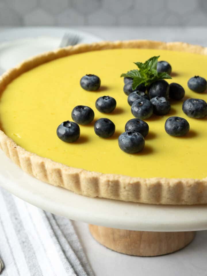 side view of lemon tart on a cake stand against gray tile background.