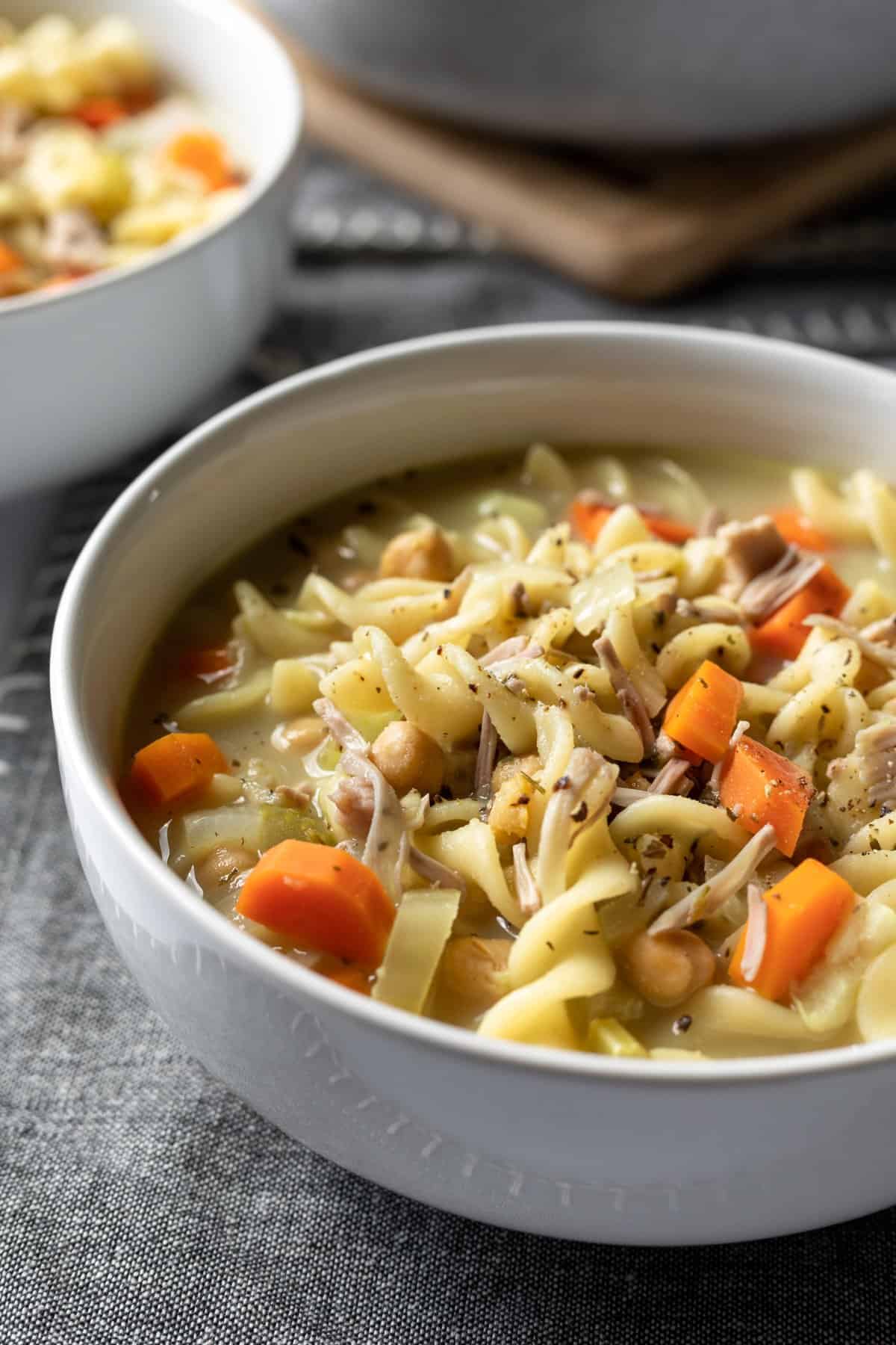 close up of bowl of soup with rotini pasta, carrots, celery, herbs and chickpeas.