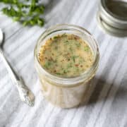 close up of herb salad dressing in a small glass jar on a gray stipe napkin.
