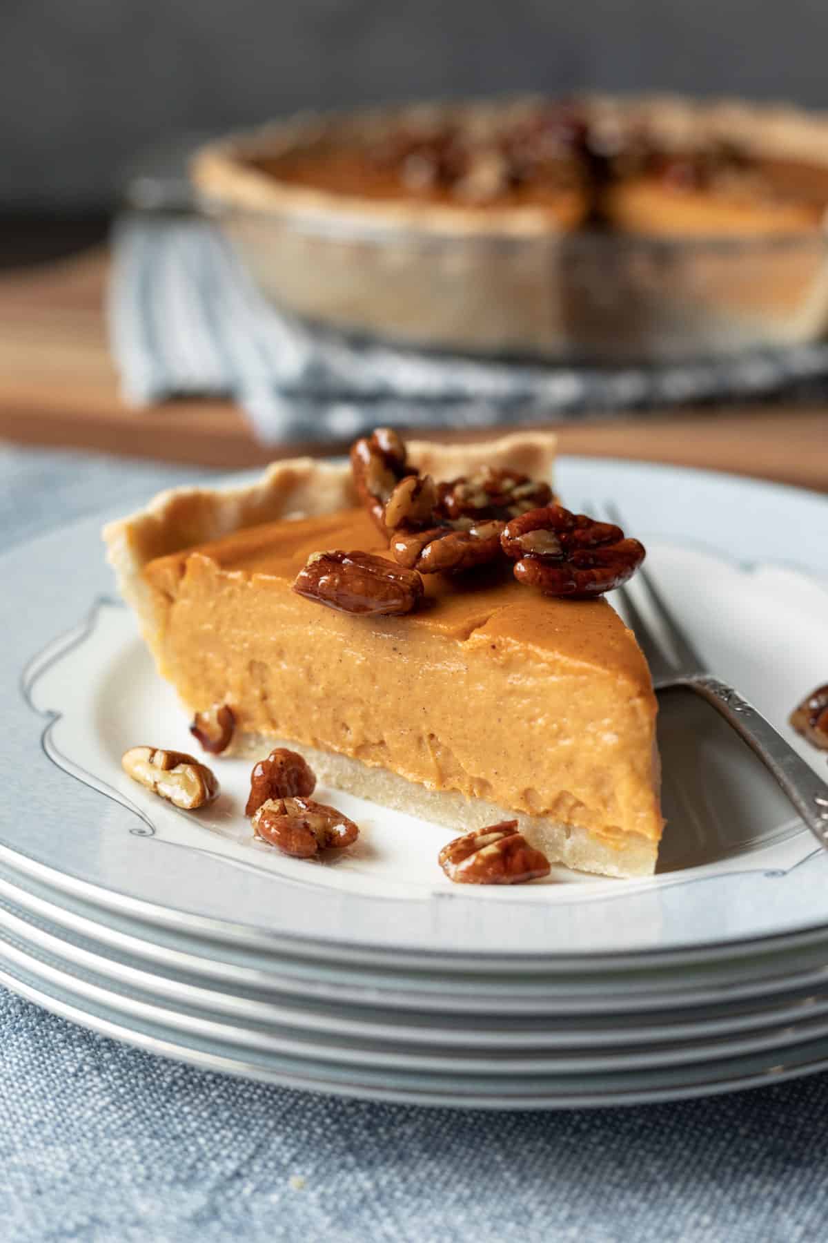 A slice of sweet potato pie on a stack of white dishes, garnished with pecans.