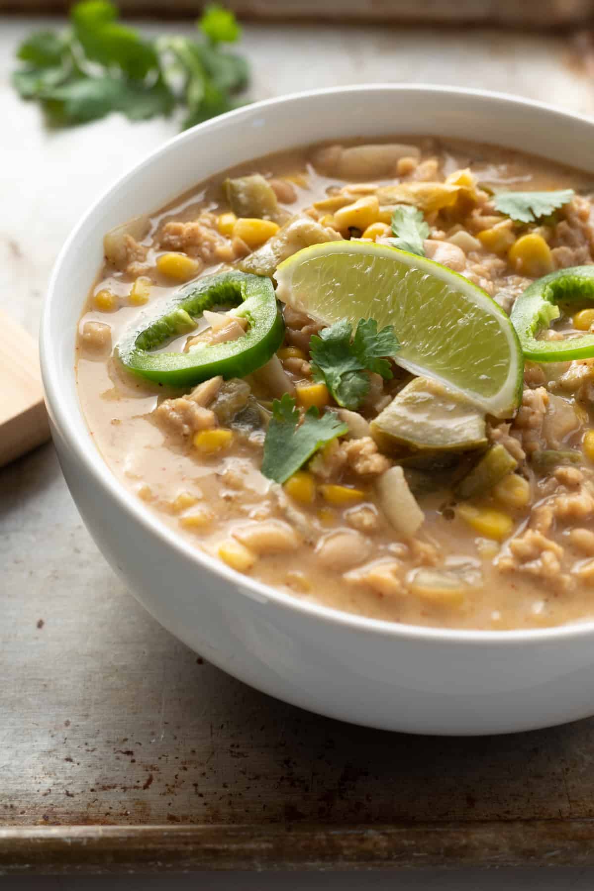 backlit photo of creamy white chili topped with sliced jalapeño and lime.