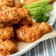 Buffalo seitan wings on a serving platter with celery in background.