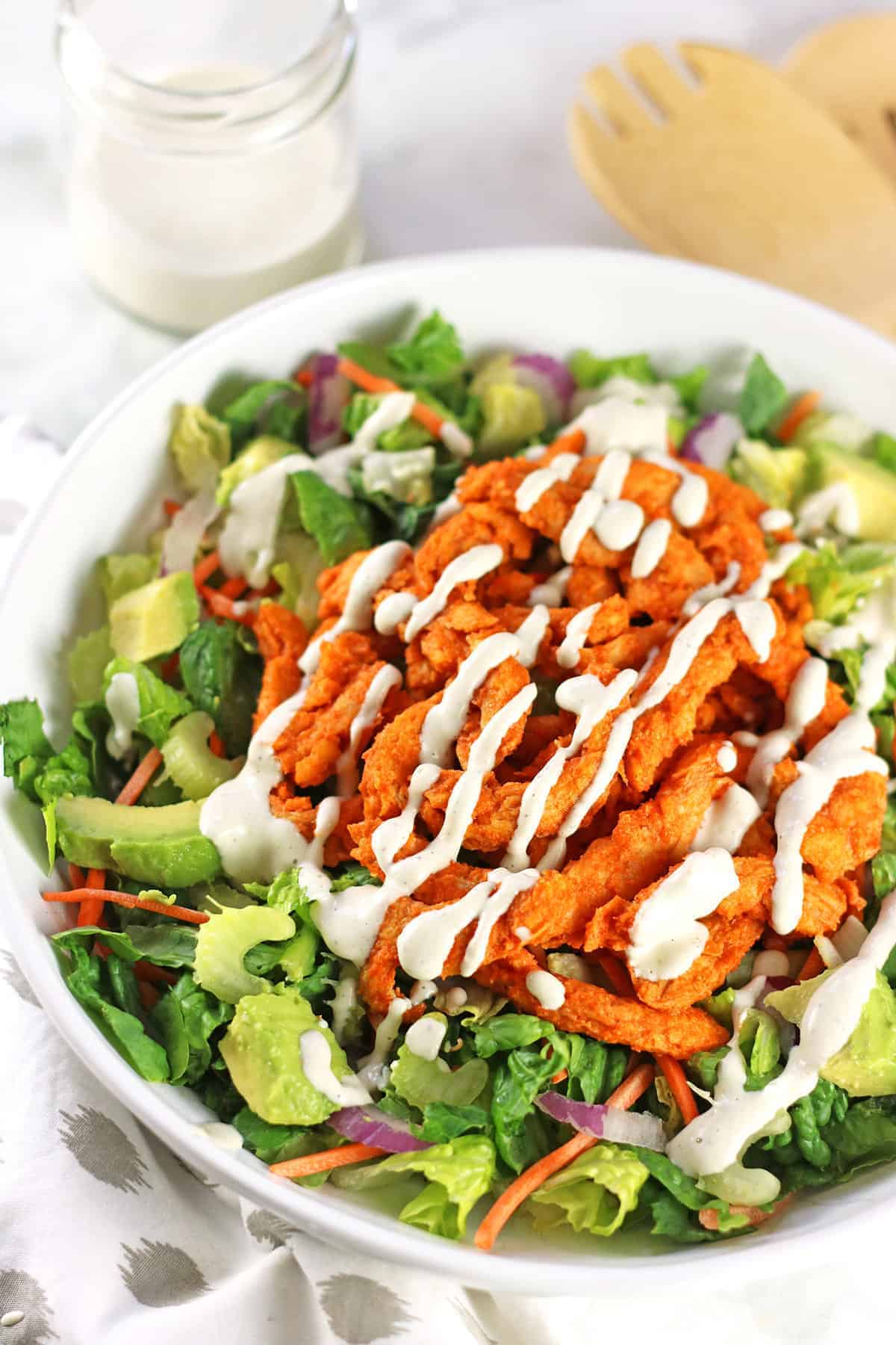 bright photo of a green salad topped with buffalo strips and avocado.