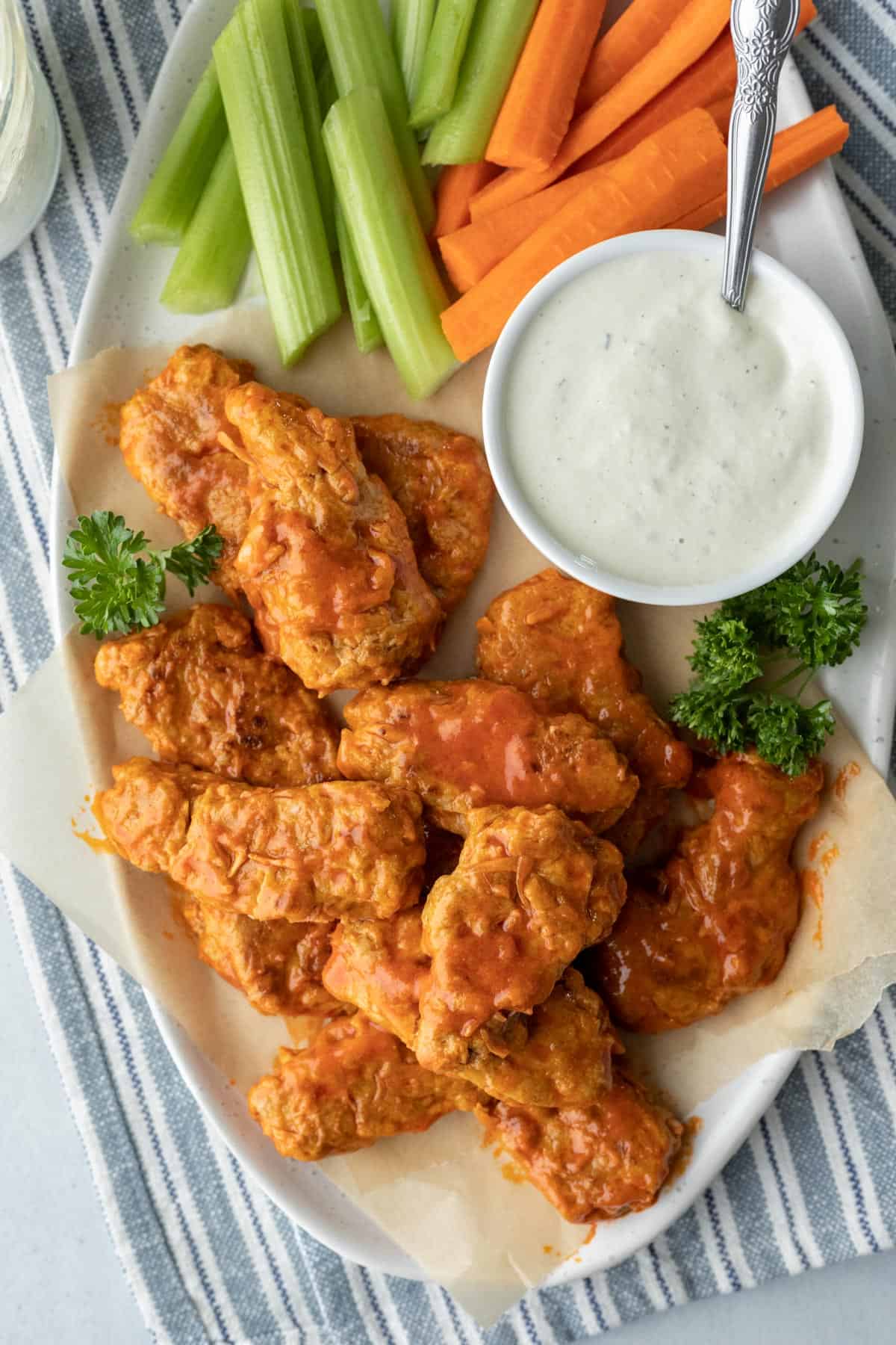Vegan chicken wings coated in sauce on a platter with vegan ranch, celery, and carrots.