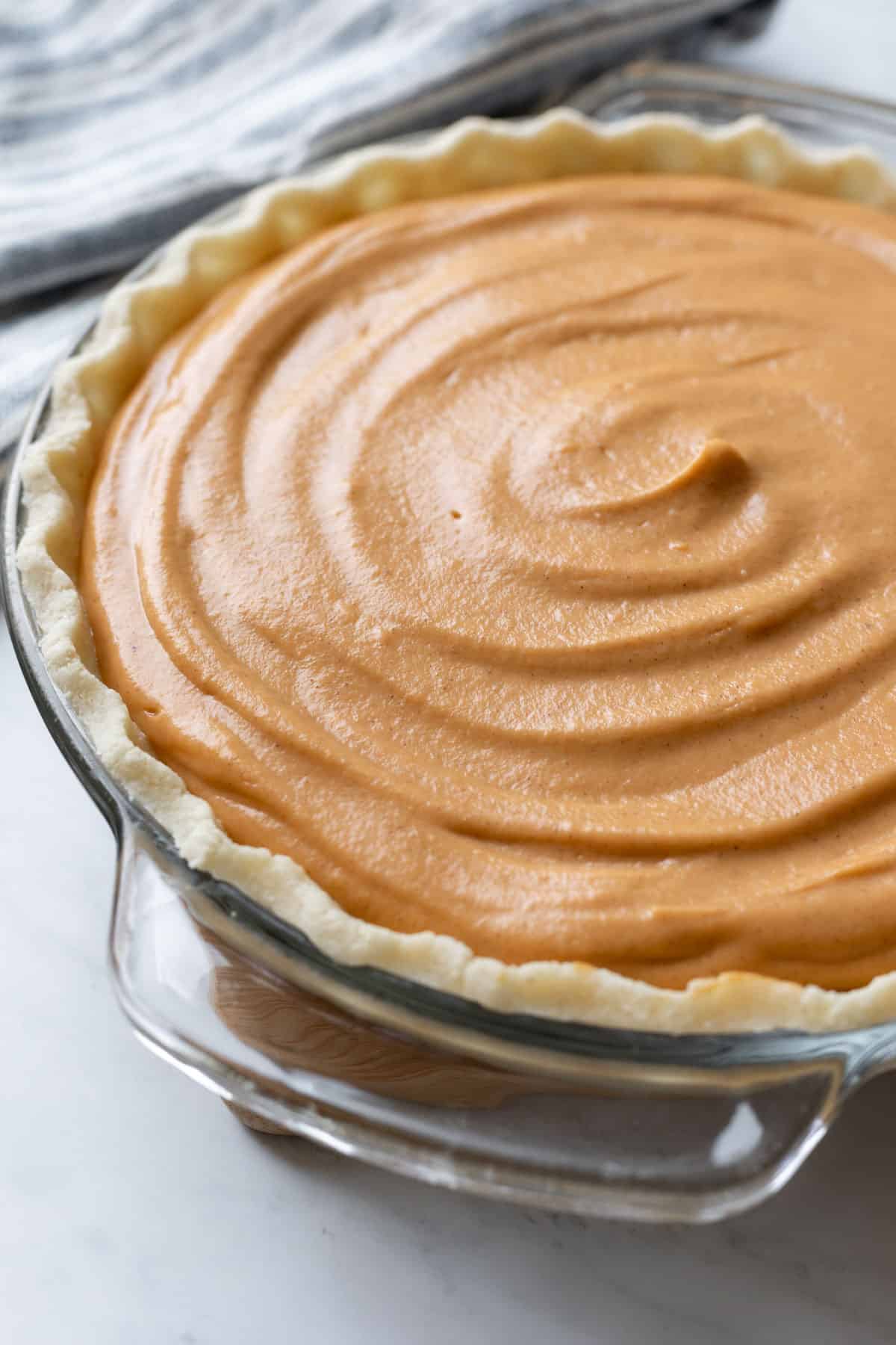 Beautiful orange sweet potato pie filling spread in pie crust and ready to be baked.