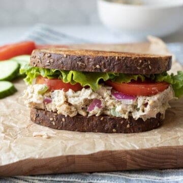 vegan sandwich topped with lettuce and tomato resting on a serving board.