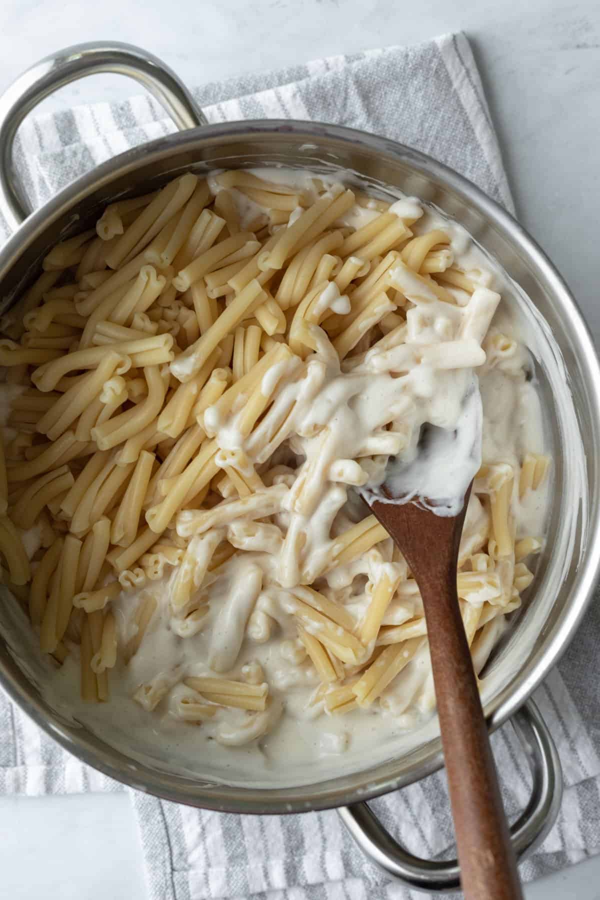 tossing pasta with creamy sauce in pot.